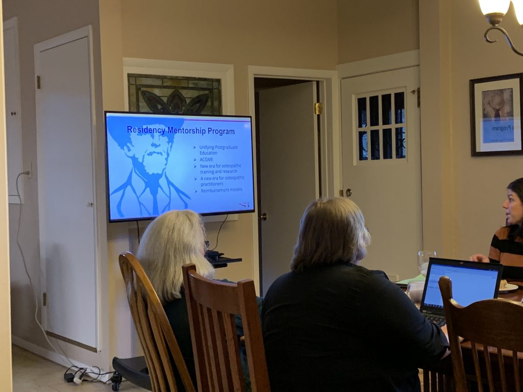 A number of people sit around a table looking at a presentation being displayed on a television.